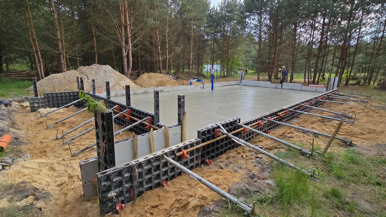 Świeżo zabetonowana płyta fundamentowa w szalunku systemowym na działce w lesie
