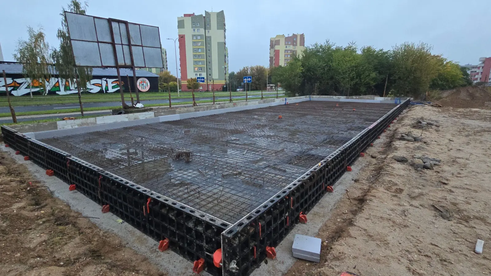 Zbrojenie płyty fundamentowej w szalunku systemowym, w tle bloki mieszkalne
