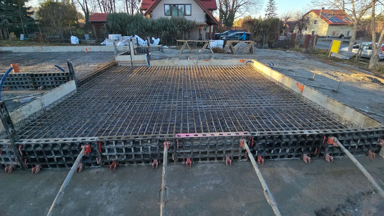 Zbrojenie płyty fundamentowej w szalunku systemowym podpartym zastrzałami, w tle domy jednorodzinne